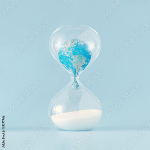 Fotografie Close-up of planet Earth melting in hourglass on pastel blue background