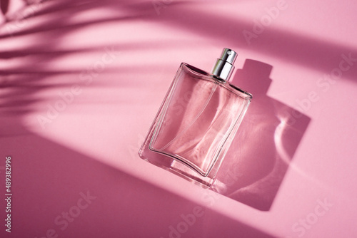 Transparent bottle of perfume on a pink background. Fragrance presentation with daylight.