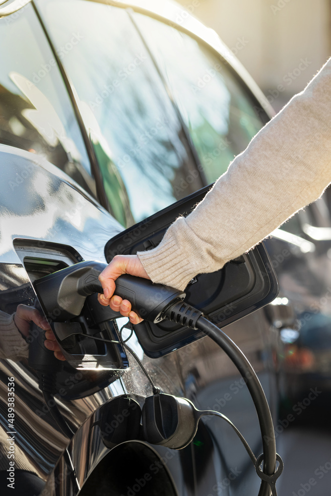Cropped view woman holding conector plugging in hands to recharge electric car Cropped view woman holding conector plugging in hands to recharge electric car