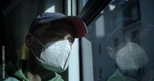 A man looks thoughtfully out the window on a bus or tram wearing a breathing mask