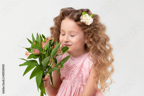 portrait little beautiful cute curls blonde girl sniff, enjoy with bouquet astromeria flowers in hands. spring holiday kid concept, international women's day, March 8, mother's day. photo