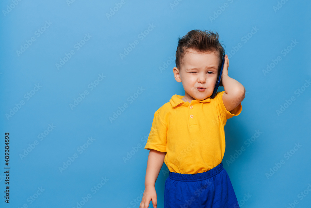 A little boy is talking on a mobile phone. Studio photo on a blue background. A little boy is talking on a mobile phone. Studio photo on a blue background.