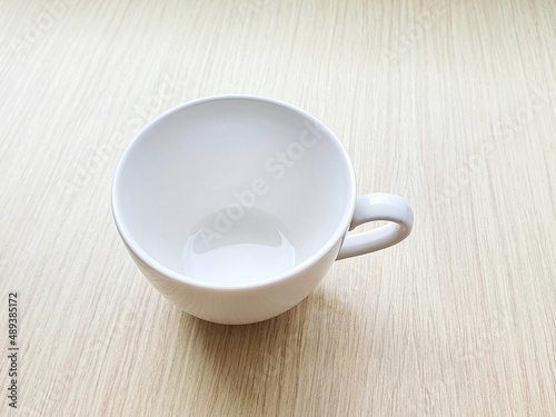 Empty white ceramic mug (eardrum) placed on a wooden table. A mug for hot beverages such as coffee, tea, soy milk, chocolate or milk. 
