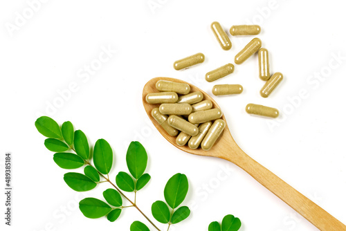Moringa oleifera capsule on wooden spoon with moringa leaf isolated on white background.
