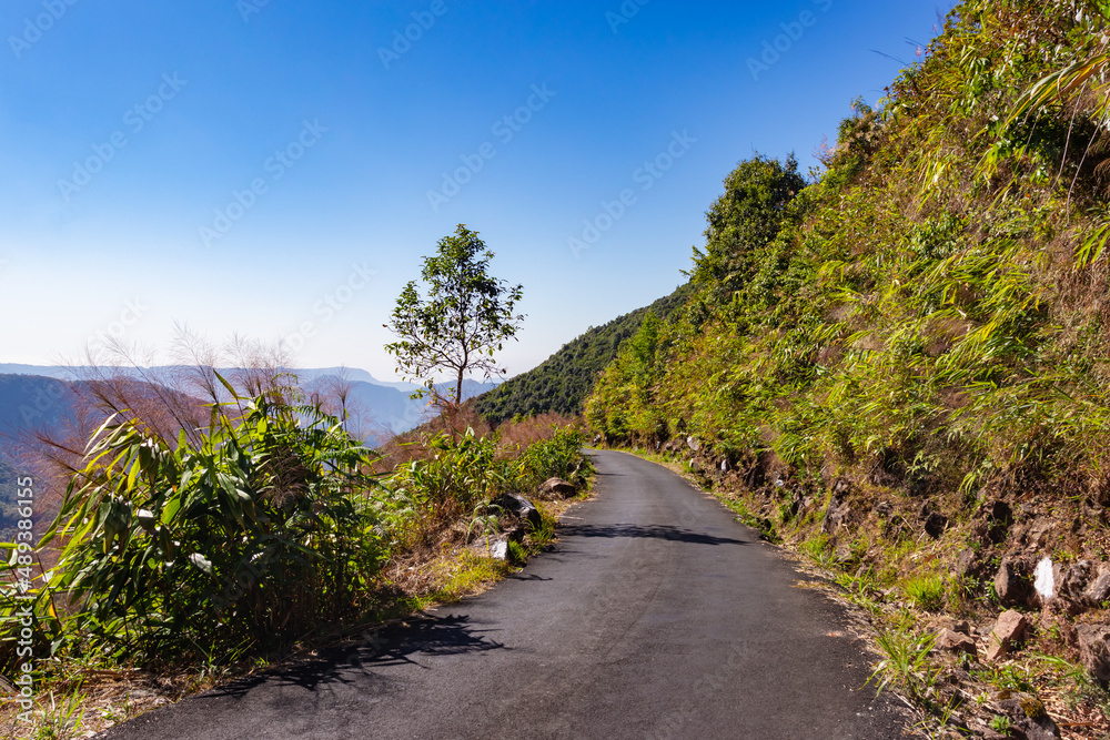 isolated mountain tarmac road with forests and bright blue sky at morning