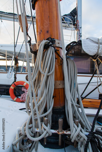 Part of the mast of a sailing yacht, with multi-colored ropes for fastening and a winch mechanism.