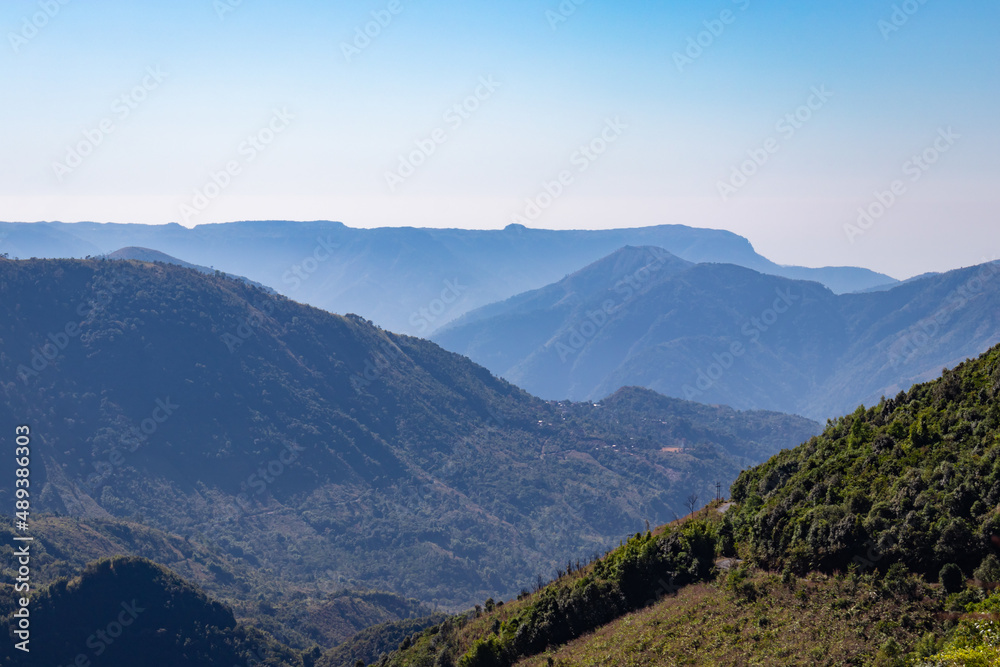 misty mountain range covered with forests and bright blue sky at morning