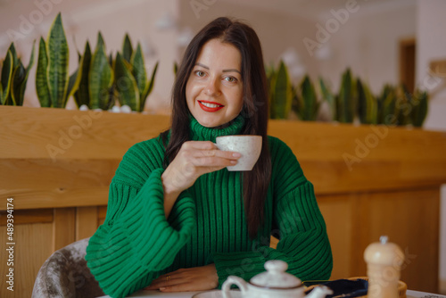 Smiling woman drinks coffee sitting at the table in cafe