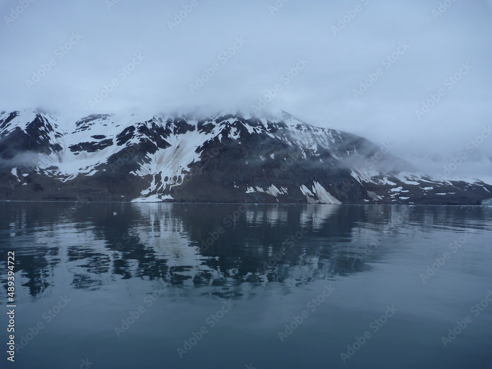 malownicze ośnieżone góry we mgle odbijające się w tafli wody w regionie svalbard na arktyce