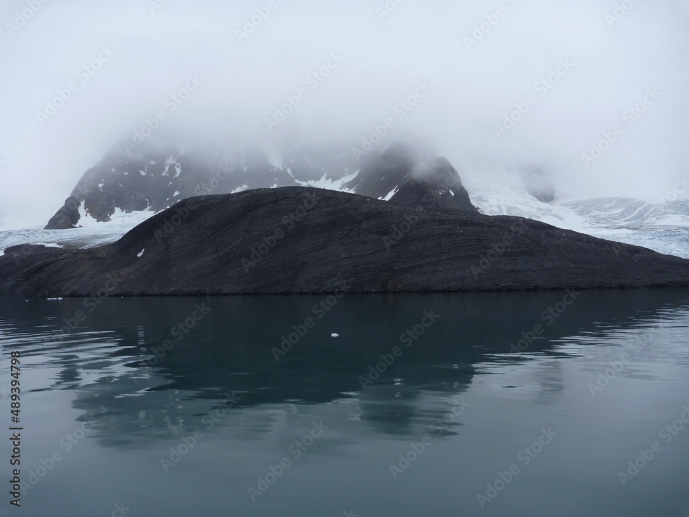 malownicze ośnieżone góry we mgle odbijające się w tafli wody w regionie svalbard na arktyce