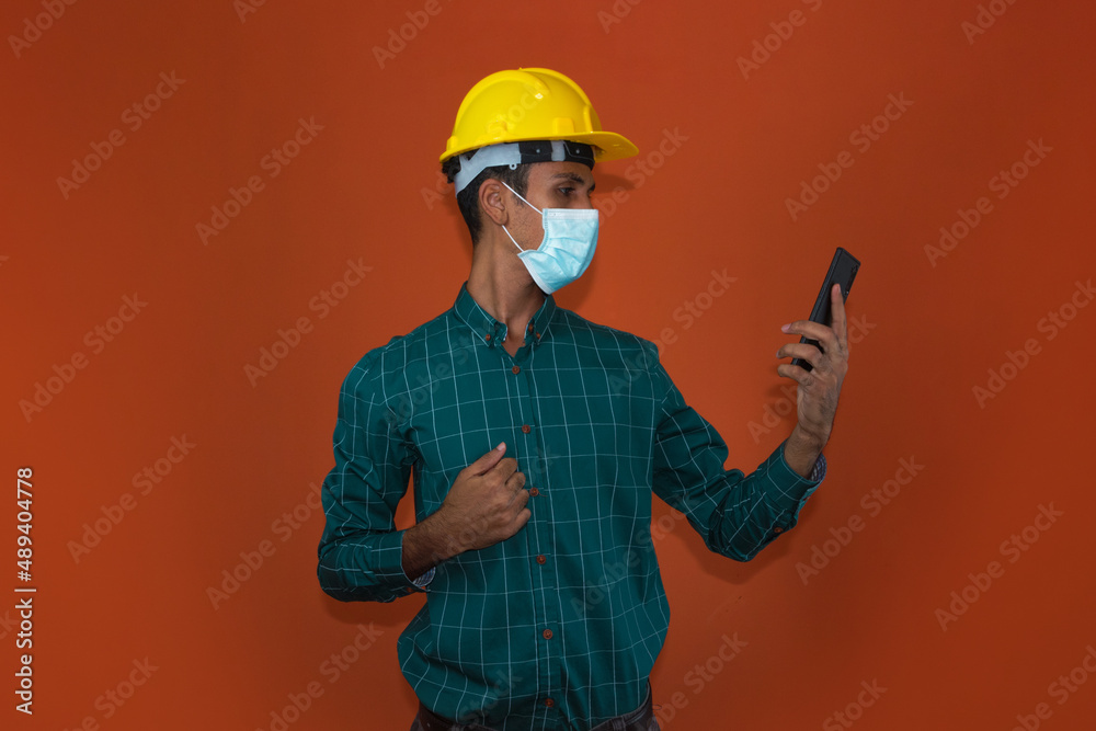 Engineer, architect or worker with yellow helmet and pandemic mask isolated on white background. Engeneer at work talking on the cell phone.