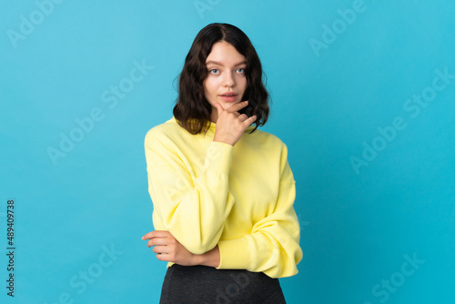 Teenager Ukrainian girl isolated on blue background thinking