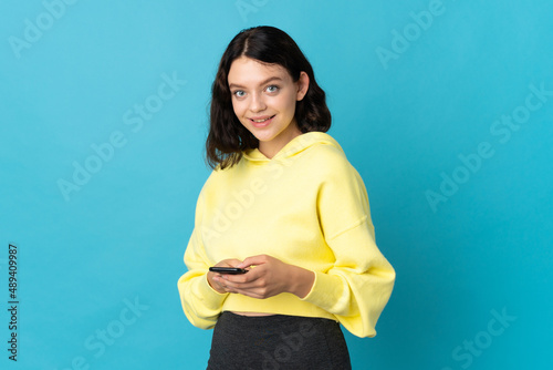 Teenager Ukrainian girl isolated on blue background sending a message with the mobile
