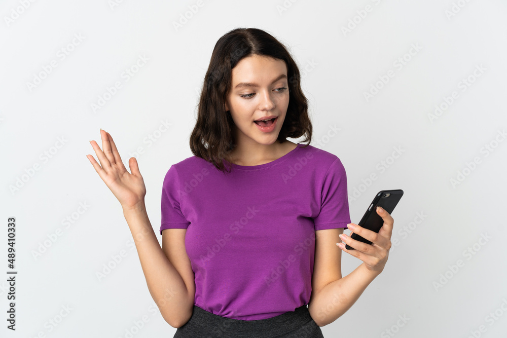 Teenager Ukrainian girl isolated on white background looking at the camera while using the mobile with surprised expression Teenager Ukrainian girl isolated on white background looking at the camera while using the mobile with surprised expression