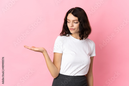 Teenager Ukrainian girl isolated on pink background holding copyspace with doubts © luismolinero