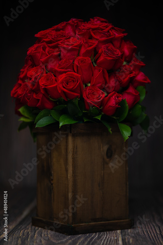 beautiful romantic photo of a bouquet of red roses with green leaves in a wooden vase, on wooden background, with a dramatic light, a surprise for lovers, a surprise for Valentine's Day, a gift, love