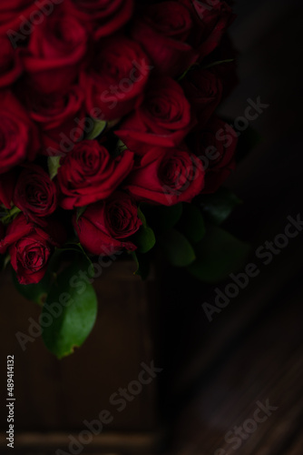 beautiful romantic photo of a bouquet of red roses with green leaves in a wooden pot, on balck background, with a dramatic light, a surprise for lovers, a surprise for Valentine's Day, a gift, love