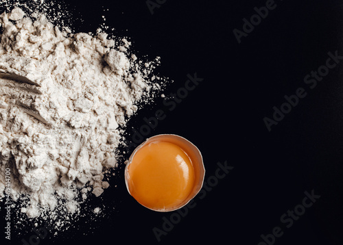 broken chicken egg in the shell next to the flour on a black background