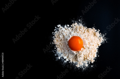 bright yolk of a chicken egg in a hill of flour on a dark background