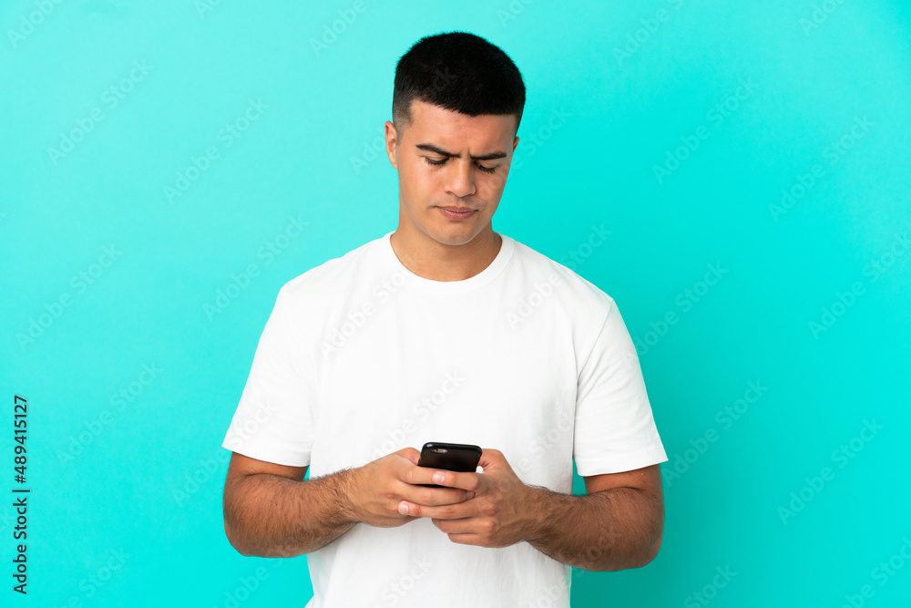Young handsome man over isolated blue background using mobile phone Young handsome man over isolated blue background using mobile phone