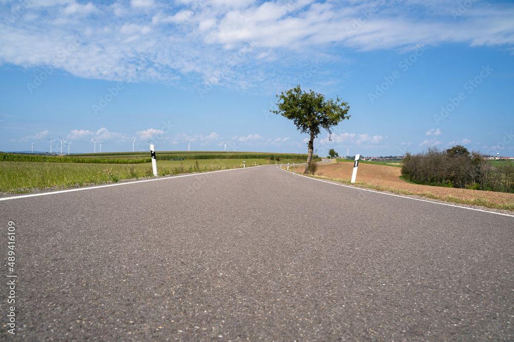 Low angle view of long asphalted road in the landscape with nice blue sky in summertime