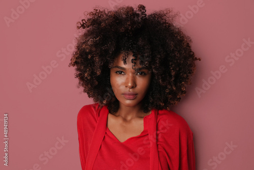 Attractive African American woman with curly hair posing on pink background.