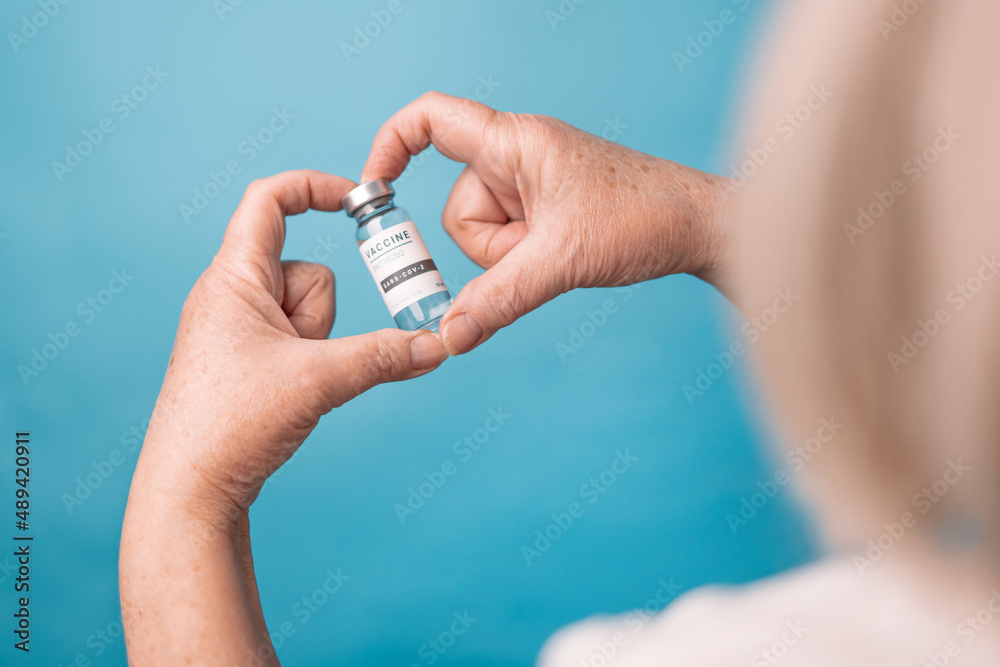Naklejka premium Woman hands hold vial of Covid - 19 vaccine on blue background
