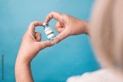 Woman hands hold vial of Covid - 19 vaccine on blue background