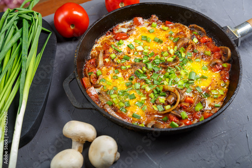 Shakshuka in a frying pan on a gray background next to vegetables.