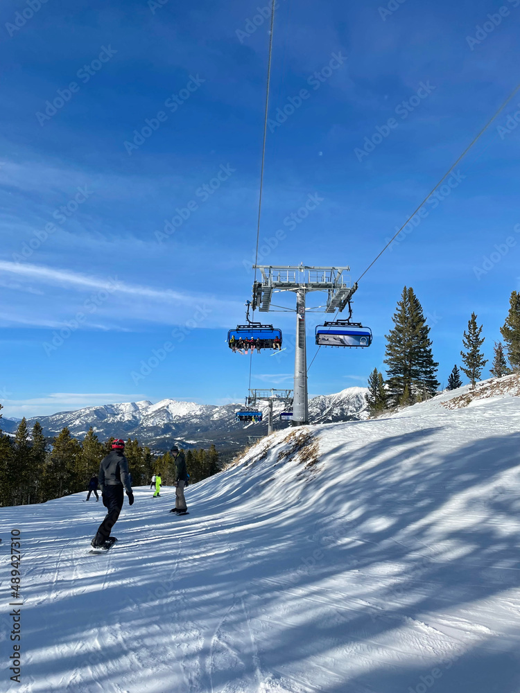 Scenic view of snowboader, chairlift and snow covered slopes at Big Sky Ski Resort in Montana on a sunny winter day