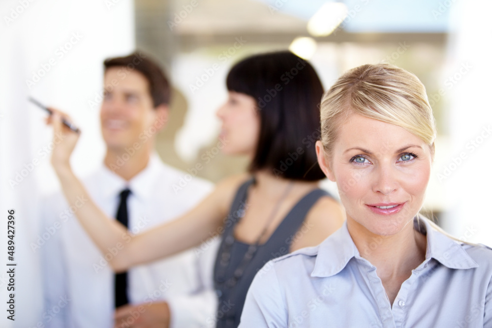 Shes got what it takes. Portrait of a pretty businesswoman smiling - blurred colleagues in the background.