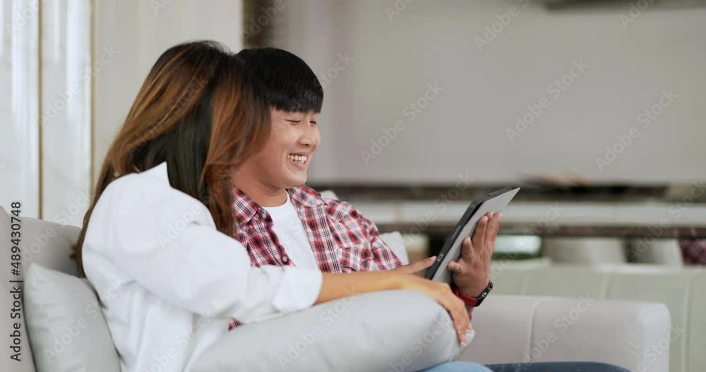 Slow motion shot, Close up, Attractive Young couple sitting on sofa in living room at home use tablet watching funny movie, talking and laughing together with happiness, happy family concept Slow motion shot, Close up, Attractive Young couple sitting on sofa in living room at home use tablet watching funny movie, talking and laughing together with happiness, happy family concept