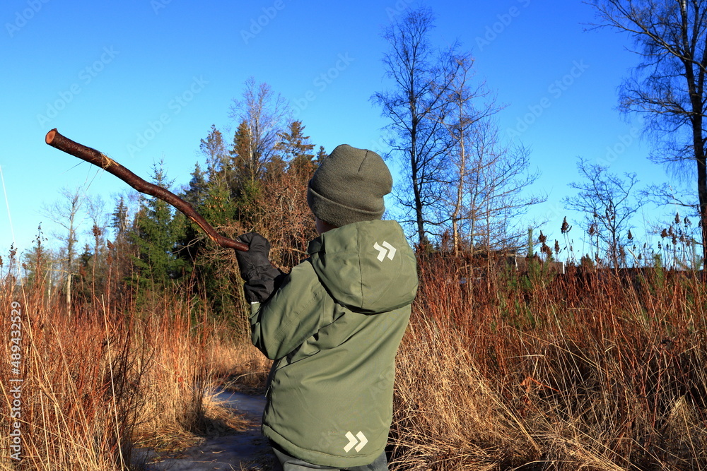 Boy with a stick in nature. Landscape photo during the month of February. Sunny and nice weather outside. Concept of exploring environment. Hat or cap. Stockholm, Sweden, Scandinavia, Europe. Boy with a stick in nature. Landscape photo during the month of February. Sunny and nice weather outside. Concept of exploring environment. Hat or cap. Stockholm, Sweden, Scandinavia, Europe.