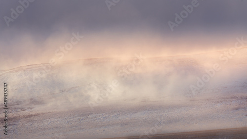 Winter background. Snow blows over a hillside in Pincher Creek, Alberta on a cold winter day as the setting sun peaks over the horizon. 