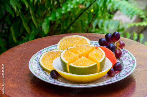 background, citrus, color, dessert, diet, eating, food, fresh, freshness, fruit, gourmet, green, ingredient, juicy, lunch, natural, nasliced orange, grapes and papaya served on a table in the garden.