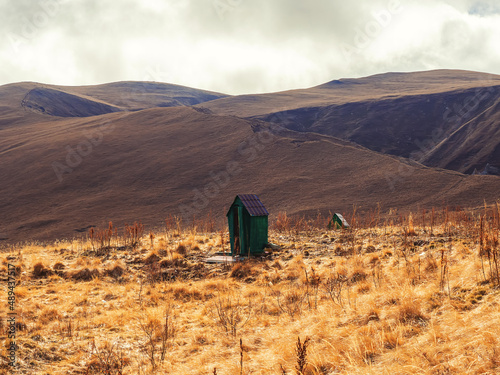 In the highlands, in the middle of a red autumn field, there is a wooden green outdoor toilet. photo