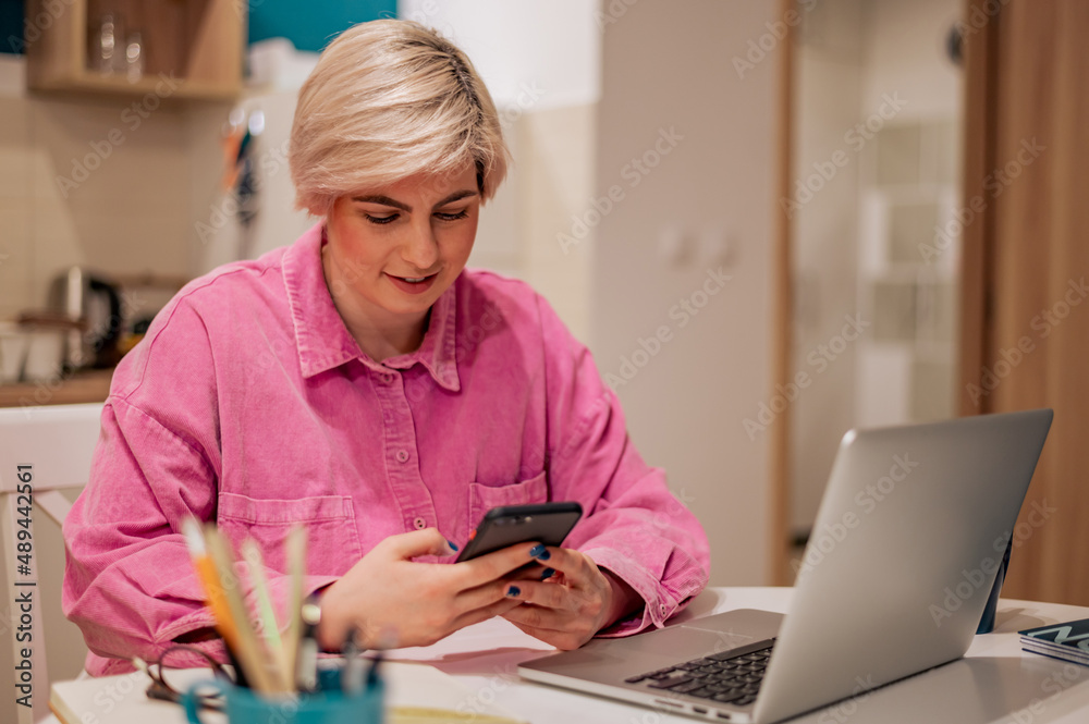 Woman with short hair using her smartphone and a modern laptop at home Woman with short hair using her smartphone and a modern laptop at home