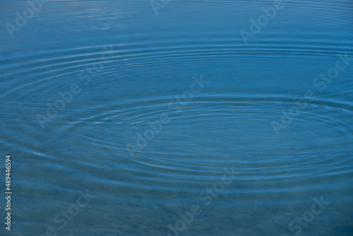 Background from the surface of a body of water, on which small waves spread out in a circle, in the blue water