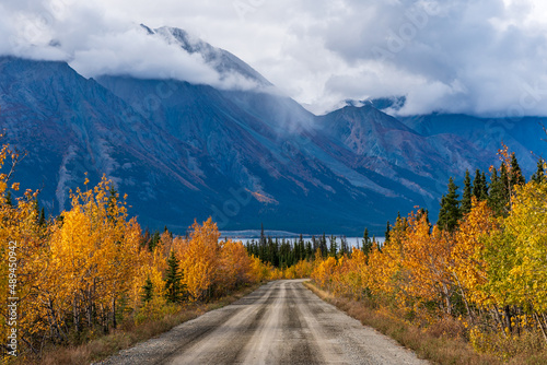 Dirt road headed to mountain landscape in northern Canada during September, fall season with golden trees covering the scenic view. 