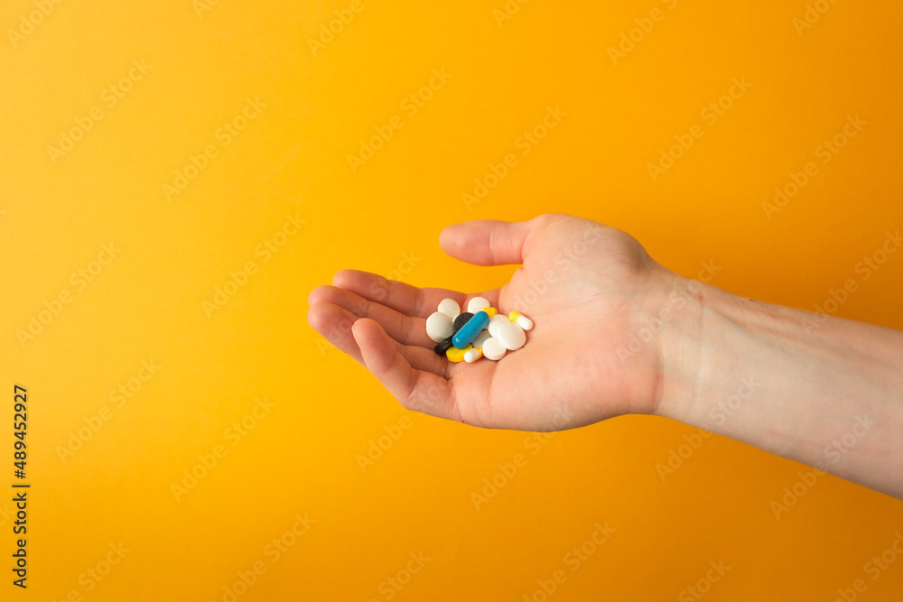 Man's palm holds a handful of different multicolored pills, capsules and drops. Yellow background. Health care concept. Man's palm holds a handful of different multicolored pills, capsules and drops. Yellow background. Health care concept.
