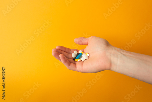 Man's palm holds a handful of different multicolored pills, capsules and drops. Yellow background. Health care concept.