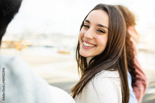 Happy young pretty woman looking at camera while walking with friends outdoors - Positive young female smiling at camera