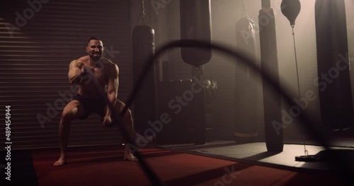 A Heavyweight Hispanic Bodybuilder / Weightlifter Battle Ropes In A Crossfit Gym. Shot In A Crossfit Boxing Gym With Low Key Lighting And A Scattering Of Haze. Captured On Red Digital Cinema Camera 