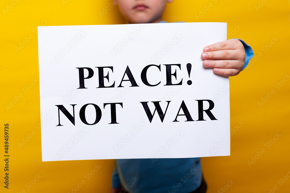 A child in a blue T shirt holds a poster with appeals for peace on a yellow background. no face, close-up A child in a blue T shirt holds a poster with appeals for peace on a yellow background. no face, close-up