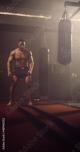 A Vertical Video Of A Hispanic Bodybuilder Exercising Battle Ropes In An MMA Gym. Shot In A Crossfit Boxing Gym With Low Key Lighting And A Scattering Of Haze. Captured On Red Digital Cinema Camera 