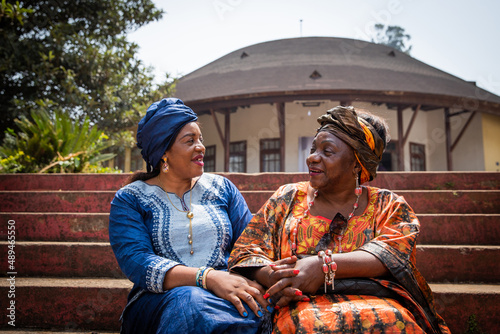 Two African women are conversing sitting on the stairs, they are both dressed in traditional clothes photo
