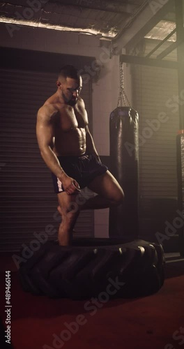 A Vertical Video Of A Hispanic Bodybuilder Doing A Tyre Walk In An MMA Gym. Shot In A Crossfit Boxing Gym With Low Key Lighting And A Scattering Of Haze. Captured On Red Digital Cinema Camera 