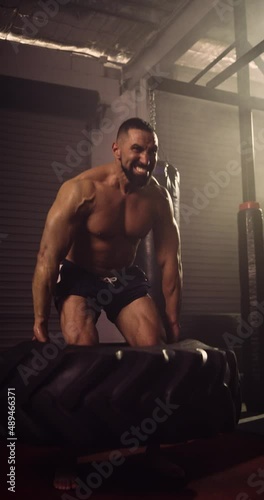 A Vertical Video Of A Hispanic Bodybuilder Exercising, Farmer Tyre Walk In A Gym. Shot In A Crossfit Boxing Gym With Low Key Lighting And A Scattering Of Haze. Captured On Red Digital Cinema Camera 