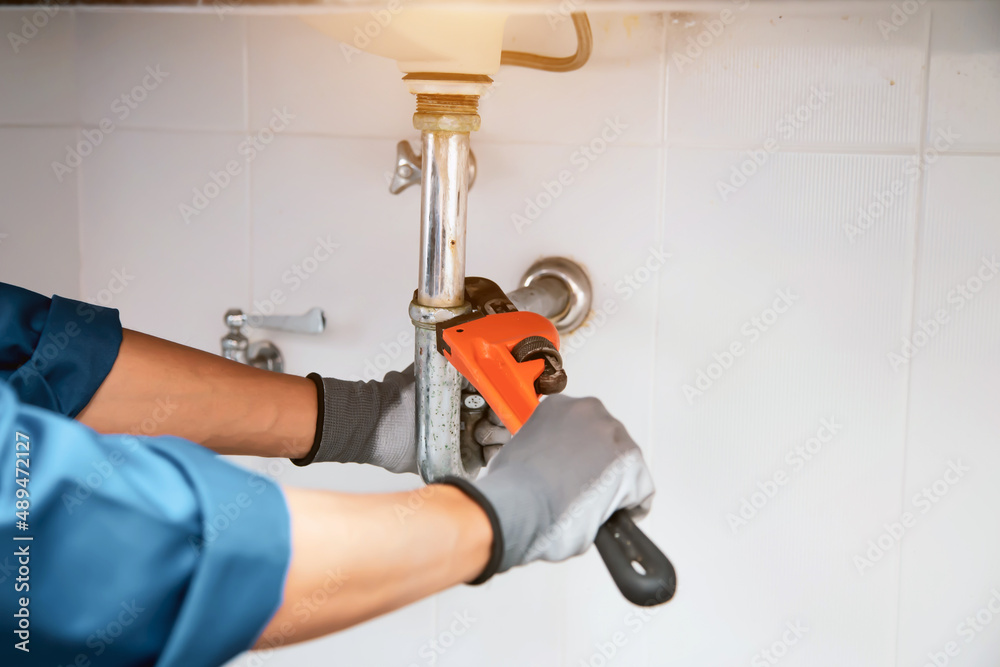 Technician plumber using a wrench to repair a water pipe under the sink. Concept of maintenance, fix water plumbing leaks, replace the kitchen sink drain, cleaning clogged pipes is dirty or rusty. Technician plumber using a wrench to repair a water pipe under the sink. Concept of maintenance, fix water plumbing leaks, replace the kitchen sink drain, cleaning clogged pipes is dirty or rusty.