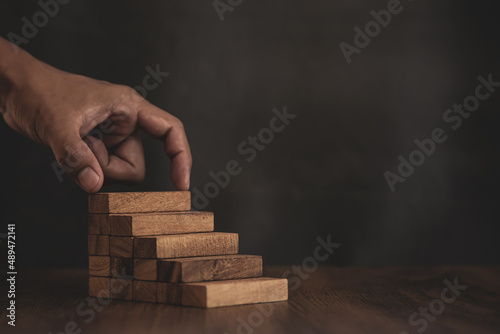 Close-up hand is placing wood block tower stacked in pyramid stair step with caution to prevent collapse or crash concepts of financial risk management and strategic planning.